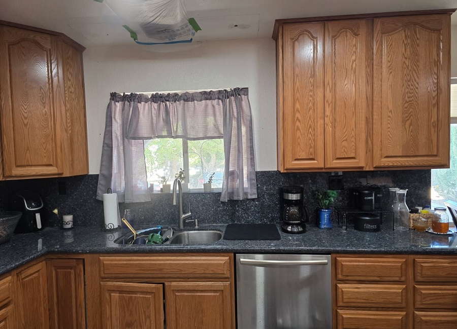 Kitchen ceiling cutout prepared for drywall repair above cabinets with protective masking in place.