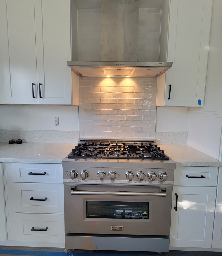White kitchen remodel with new tile backsplash, stainless range, and under-cabinet lighting.